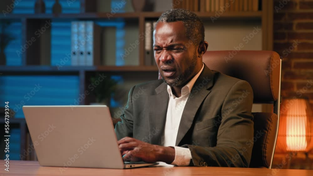 Focused businessman typing on laptop working in office sick unhealthy african american man sneezes feeling symptoms of cold suffering from allergies sneezing from dust suffers from flu feels unwell
