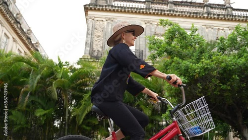 Smiling, happy, fun mature elderly woman in ethnic clothing and hat biking on the Central Avenue Paseo de Montejo with museums, restaurants, monuments and tourist attractions in Merida Yucatan Mexico.
