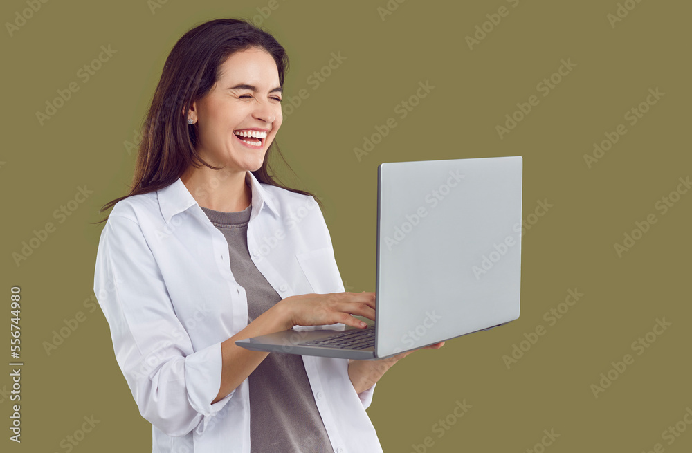 Happy laughter young woman with laptop computer in hands closes her eyes with laughter, dressed in gray T-shirt and white shirt on isolated photo. Studio portrait of joyful brunette girl with laptop. Happy laughter young woman with laptop computer in hands closes her eyes with laughter, dressed in gray T-shirt and white shirt on isolated photo. Studio portrait of joyful brunette girl with laptop.