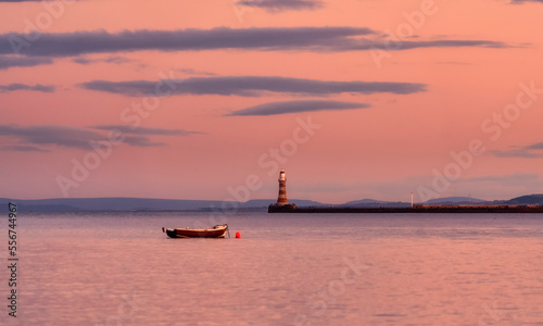 Roker Pier Lighthouse at dusk with a glowing pink sky reflected on the tranquil water and a lone rowboat moored by a buoy; Sunderland, Tyne and Wear, England photo