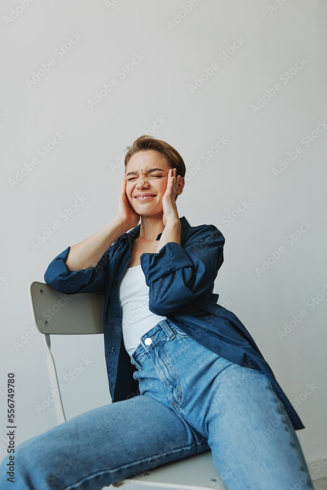 A young woman sitting in a chair at home smiling with teeth with a short haircut in jeans and a denim shirt on a white background. Girl natural poses with no filters A young woman sitting in a chair at home smiling with teeth with a short haircut in jeans and a denim shirt on a white background. Girl natural poses with no filters
