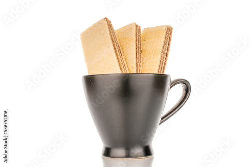 Three sweet chocolate wafers in a black ceramic cup, close-up, isolated on a white background.