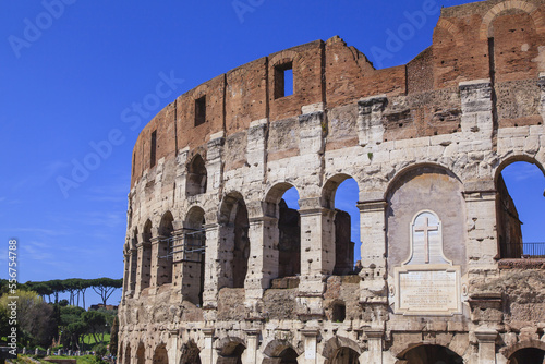 Close-up view of the iconic Colosseum against a blue sky, showing a marble plaque  above the East Entrance dedicated to Christian martyrs; Rome, Lazio, Italy photo