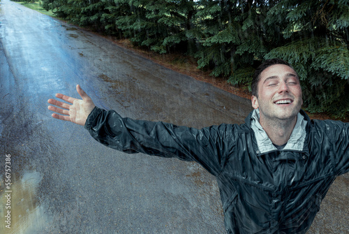 A young man stands getting doused in the rain, looking up with arms raised in surrender; Studio photo