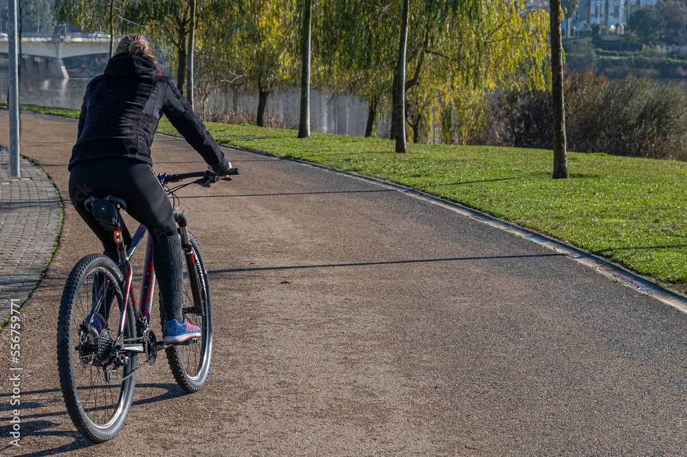 Unrecognizable Person Enjoying Daily Exercise Routine. Rear View Of A Young Woman Riding A Bicycle In The Park In The City. Young Person Keeping Fit, Healthy Lifestyle. Sports. Image with copy space Unrecognizable Person Enjoying Daily Exercise Routine. Rear View Of A Young Woman Riding A Bicycle In The Park In The City. Young Person Keeping Fit, Healthy Lifestyle. Sports. Image with copy space