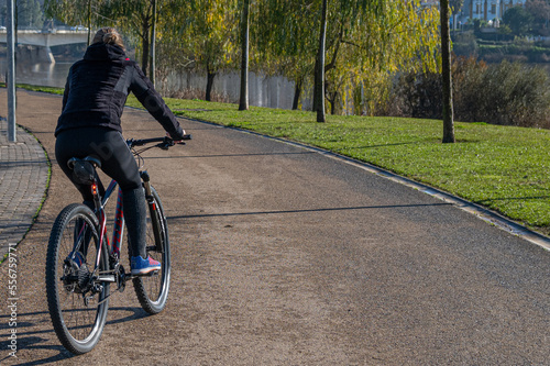 Unrecognizable Person Enjoying Daily Exercise Routine. Rear View Of A Young Woman Riding A Bicycle In The Park In The City. Young Person Keeping Fit, Healthy Lifestyle. Sports. Image with copy space