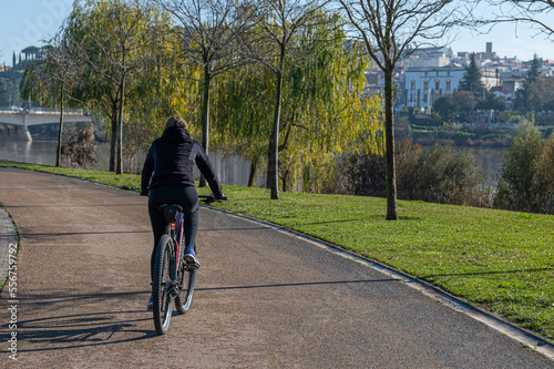 Unrecognizable Person Enjoying Daily Exercise Routine. Rear View Of A Young Woman Riding A Bicycle In The Park In The City. Young Person Keeping Fit, Healthy Lifestyle. Sports.