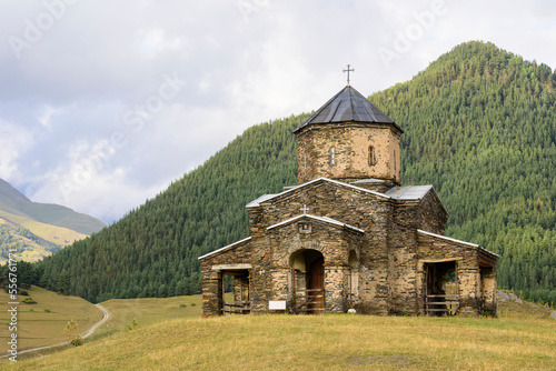 Old Church of the Holy Trinity in Shenako with the forested mountains of the Greater Caucasus in the background in the Tusheti National Park; Shenako, Kakheti, Georgia photo