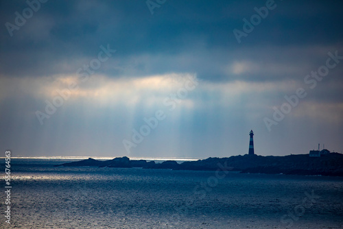 Hellisoy Lighthouse, a remote lighthouse on an island in the Western Fjords of Norway with sun rays reflecting through a stormy sky; Hordaland, Norway photo