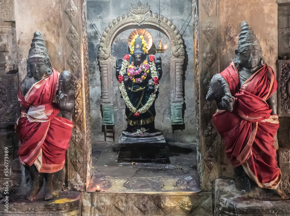 Alcove with Hindu deity statue in wall with guardian statues wrapped in silk on either side at