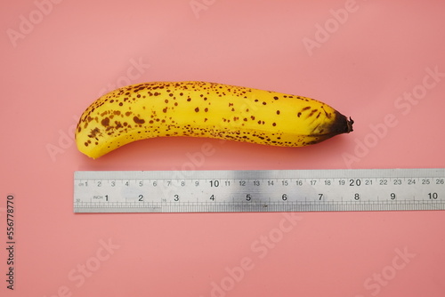 Yellow banana with measuring ruler on pink background. Male penis size concept. Flat lay, top view, copy space photo