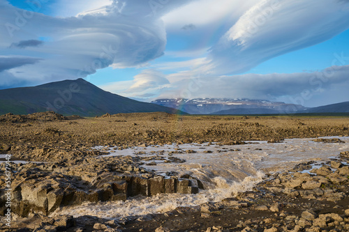 Glacial river flowing through the basalt landscape with a dramatic cloudy sky along the Kaldidalur Valley; Husafell, Nordurland Vestra, Iceland photo