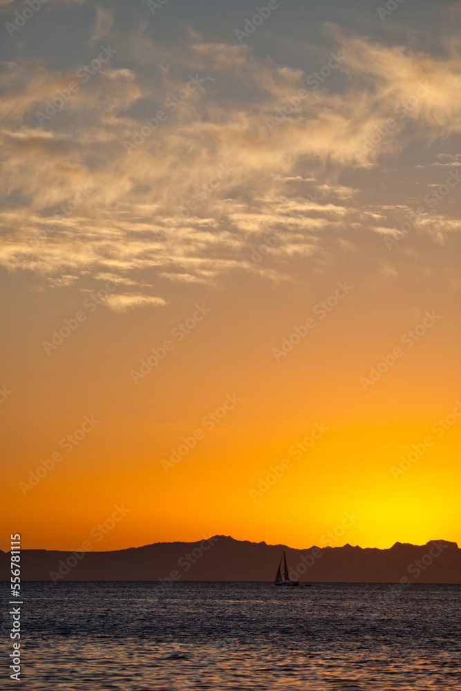 A sailboat at sunset with the Baja Peninsula in the background. A sailboat at sunset with the Baja Peninsula in the background.