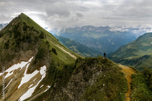 A hiker reaching a mountaintop and looking out at the magnificent vista of the alps with a cloudy sky; Feldkirch, Vorarlberg, Austria photo