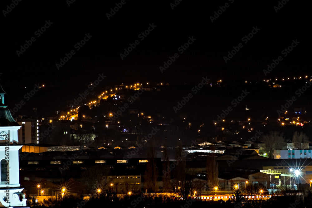 Ostrowiec Świętokrzyski nocą . Widok miasta z góry . Zabudowania starej huty , światła miasta . Oświetlona droga wspinająca się na wzgórza .