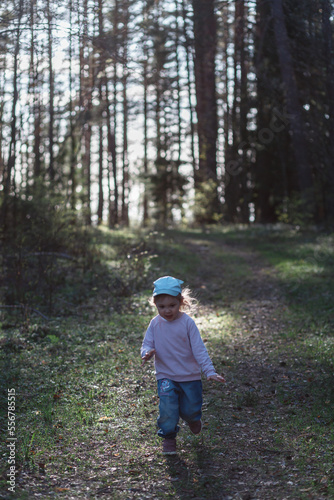 A three-year-old girl runs through a pine forest in the spring on a sunny day. Vertical orientation. © Константин Чернышов