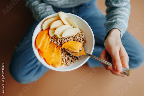 Unrecognizable person sits on the floor in his apartment and holds a spoon and plate with a healthy breakfast in hands. Healthy breakfast in hands of a health conscious person. Diet food, plant foods.