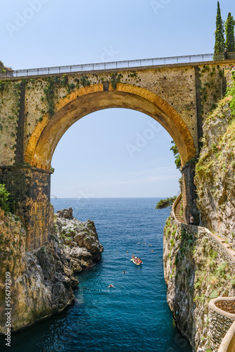 People swimming and boating under an old road bridge across the bay in Furore; Furore, Salerno, Italy