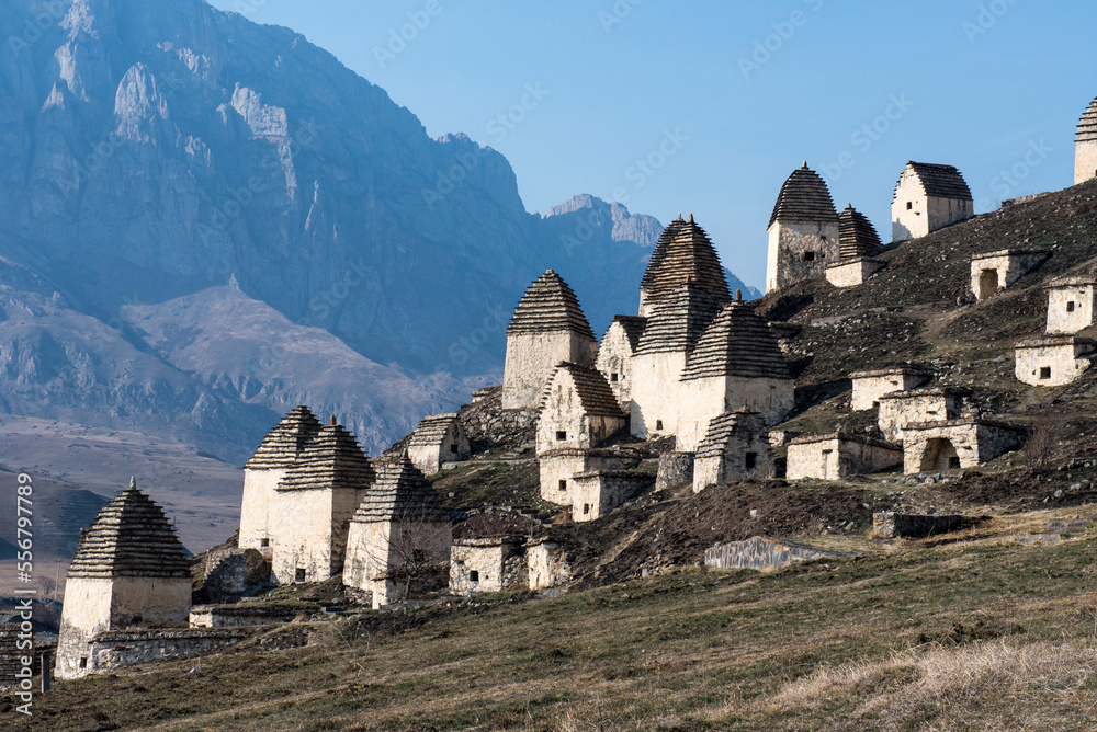 Abandoned village with traditional conical roofed shelters on the mountainside in Ingushetia with jagged mountain ridges in the background; Republic of Ingushetia, Russia Abandoned village with traditional conical roofed shelters on the mountainside in Ingushetia with jagged mountain ridges in the background; Republic of Ingushetia, Russia