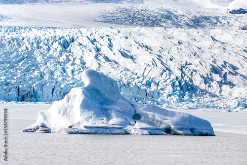 un iceberg emerge dalla laguna ghiacciata al centro dell'immagine, sullo sfondo la lingua del ghiacciaio Fjallsárlón con i crepacci ben visibili