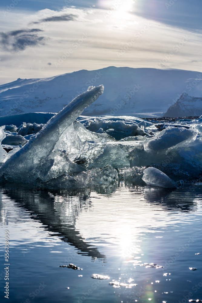 un Iceberg dalla forma strana emerge dalla laguna ghiacciata illuminata dal sole con sullo sfondo le montagne in prossimità del tramonto