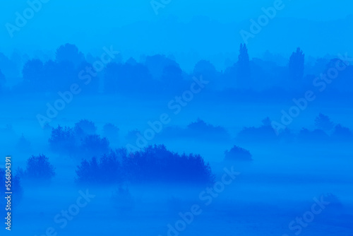 Misty dawn glowing blue across the Somerset Levels, seen from the summit of Burrow Mump, a manmade hillock at Burrowbridge, near Langport, Somerset, Great Britain; Burrowbridge, Somerset, England photo