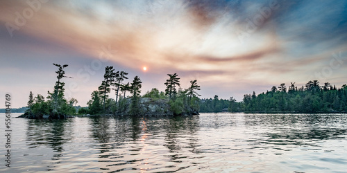 Sun glowing in clouds over a lake and forest at sunset, Lake of the Woods, Ontario; Kenora, Ontario, Canada photo