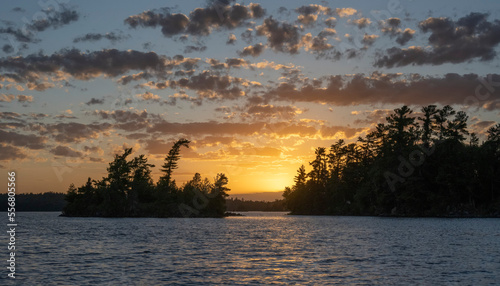 Golden sun glowing over silhouetted landscape and water at sunset, Lake of the Woods, Ontario; Kenora, Ontario, Canada