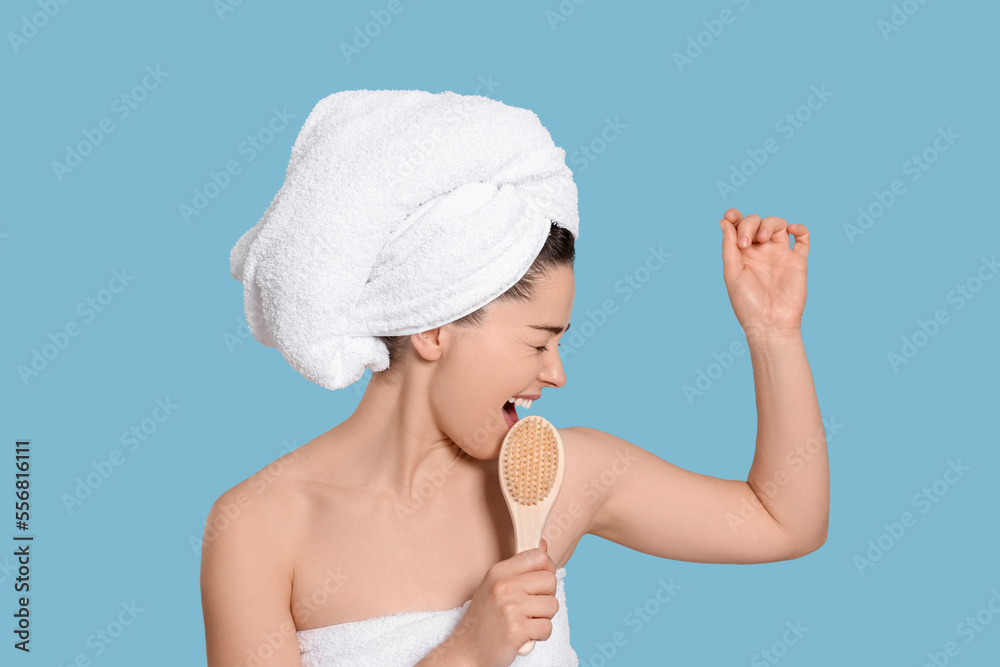 Emotional woman in towels singing into brush on light blue background. Spa treatment Emotional woman in towels singing into brush on light blue background. Spa treatment