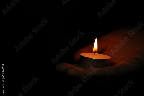 Woman holding burning candle in darkness, closeup. Space for text