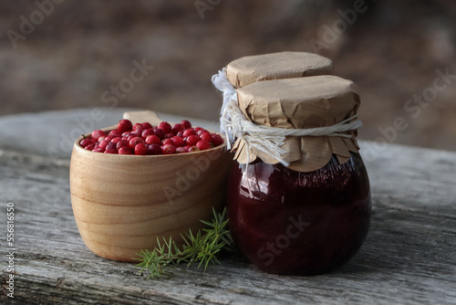 Tasty lingonberry jam in jars and cup with red berries on wooden table outdoors