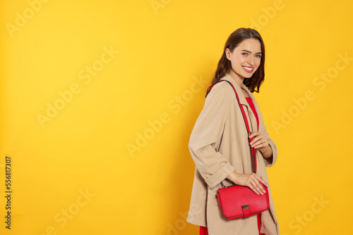 Beautiful young woman in fashionable outfit with stylish bag on yellow background, space for text © New Africa