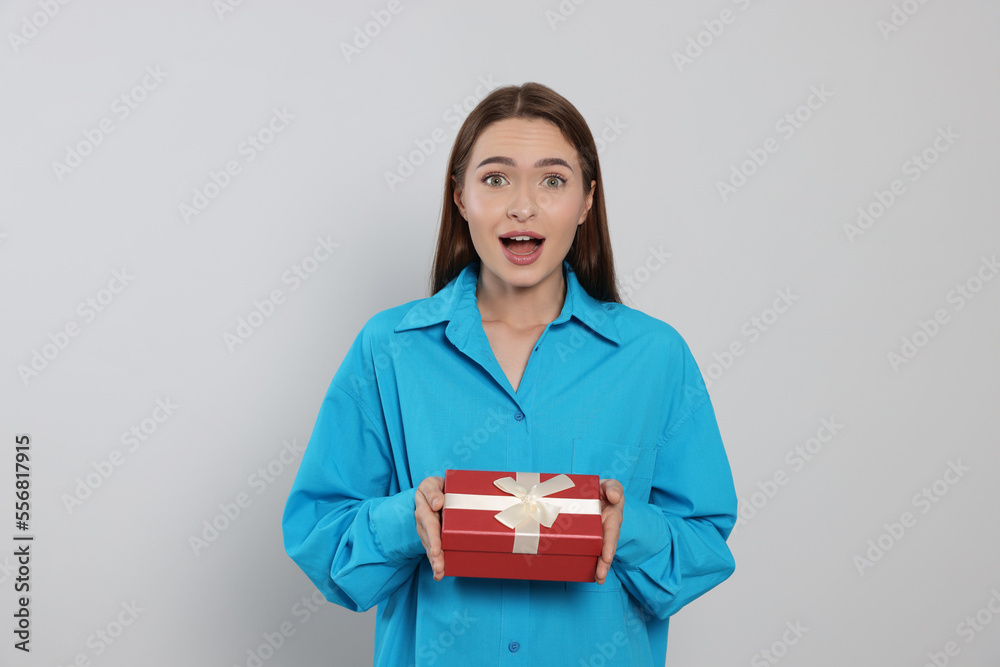 Portrait of emotional young woman with gift box on grey background Portrait of emotional young woman with gift box on grey background