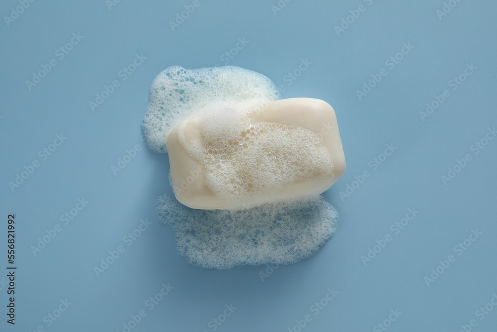 Soap bar with fluffy foam on light blue background, top view