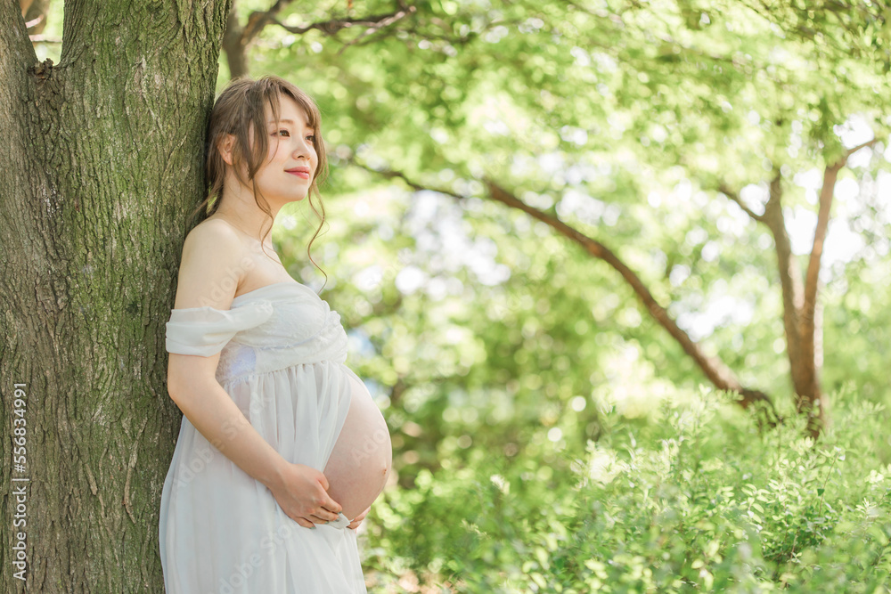 新緑の中ドレスを着てマタニティフォトの撮影をする妊婦のアジア人女性（妊娠）
