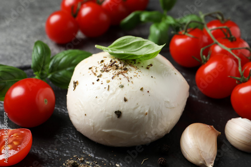 Delicious mozzarella with tomatoes and basil leaves on black table, closeup