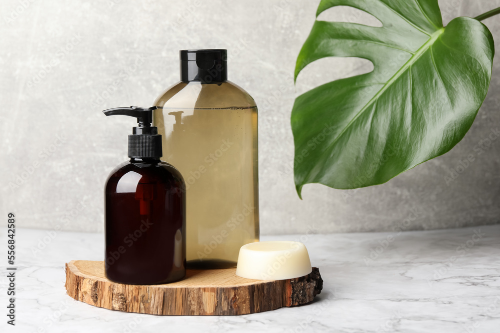 Solid shampoo bar and bottles of cosmetic product on white marble table, space for text