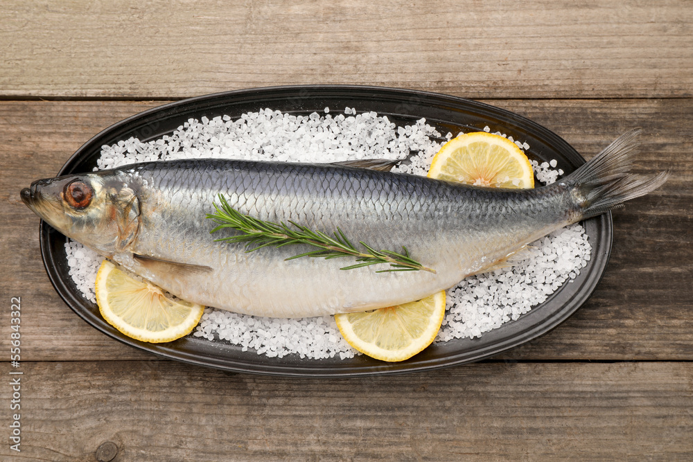 Plate with salted herring, rosemary and lemon on wooden table, top view Plate with salted herring, rosemary and lemon on wooden table, top view