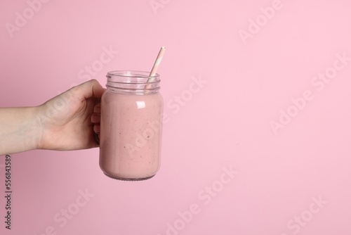 Woman holding mason jar of tasty smoothie on pink background, closeup. Space for text