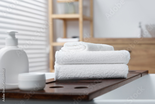 Stacked bath towels and personal care products on tub tray in bathroom