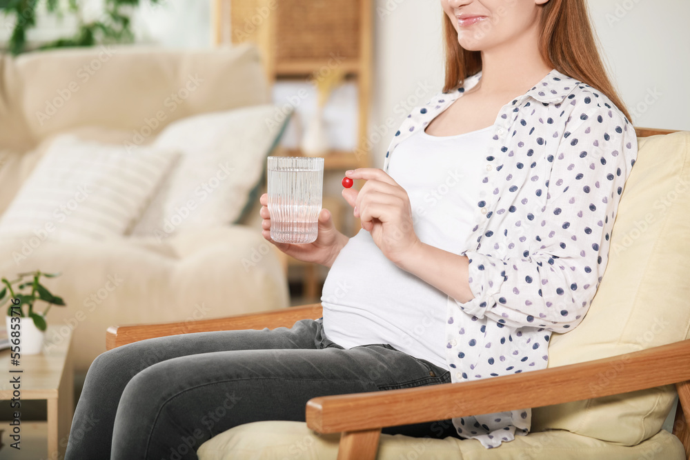 Pregnant woman holding pill and glass of water at home, closeup Pregnant woman holding pill and glass of water at home, closeup