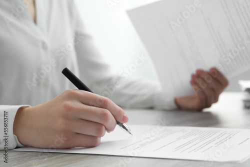 Woman signing documents at wooden table in office, closeup. Space for text