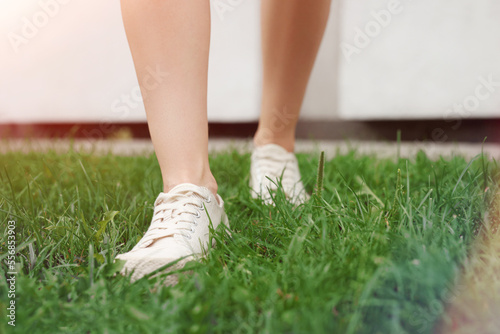 Woman in stylish sneakers walking on green grass outdoors, closeup. Space for text