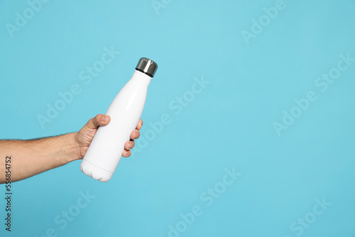 Man holding thermo bottle on light blue background, closeup. Space for text