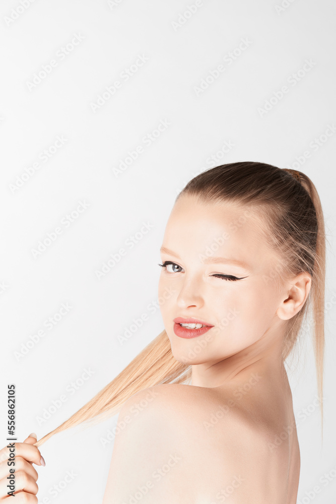 Portrait of attractive blond-haired girl with naked shoulders and high ponytail looking at camera and winking on white background Portrait of attractive blond-haired girl with naked shoulders and high ponytail looking at camera and winking on white background