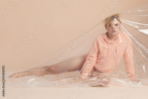 Full shot of attractive male model in pastel peach clothing covered with plastic posing on camera photo
