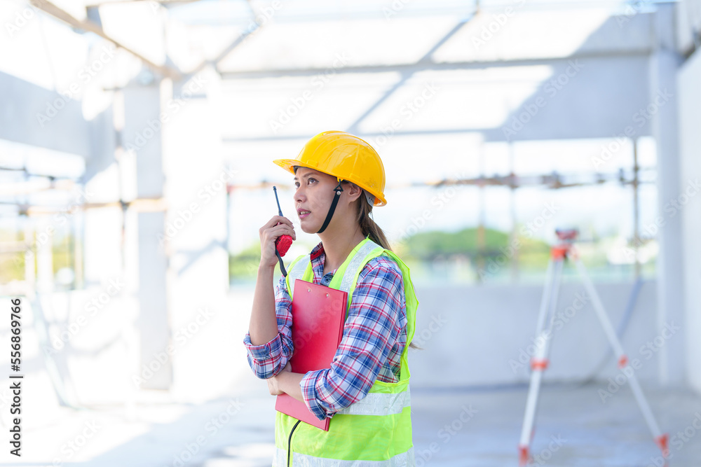 Side view of female engineer using walkie-talkie in construction site for building site survey in civil engineering project. Side view of female engineer using walkie-talkie in construction site for building site survey in civil engineering project.
