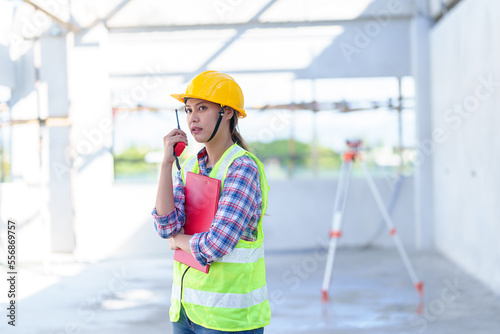 Side view of female engineer using walkie-talkie in construction site for building site survey in civil engineering project.