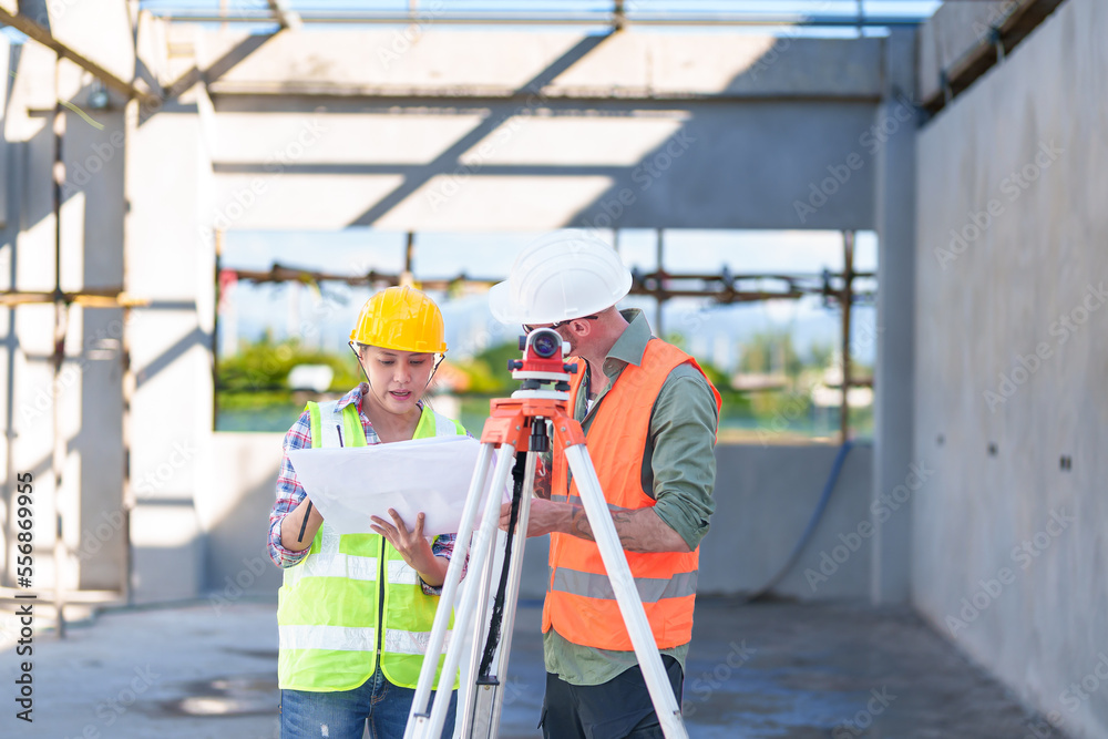 Construction Worker Using Theodolite Surveying Optical Instrument for Measuring Angles in Horizontal and Vertical Planes on Construction Site. Engineer and Architect Using blueprint Next to Surveyor.