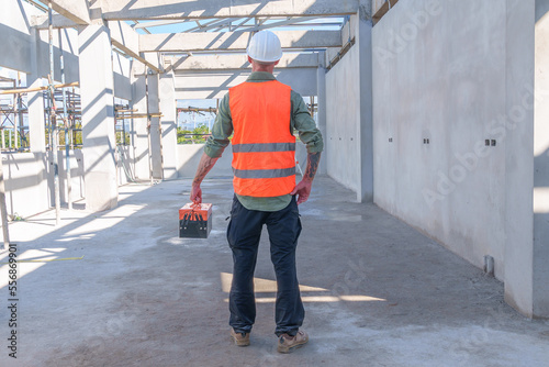 Male engineer wearing safety suit and hard hat holding toolbox and electric drill in construction site for building site survey in civil engineering project.